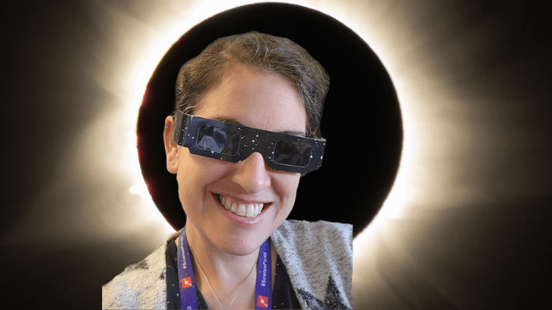 Talia with eclipse glasses on in front of an image of the eclipse