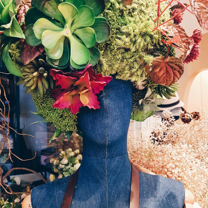 A mannequine with a hat made out of flowers and other natural items.