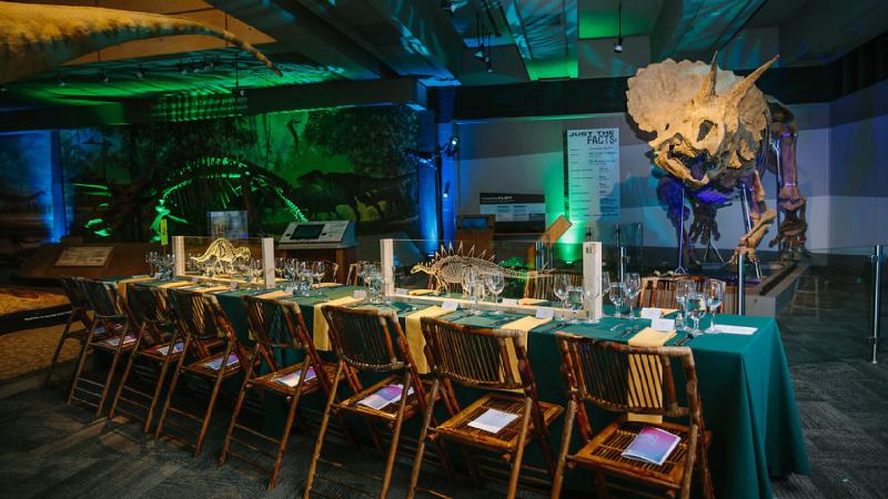 A long table set for a formal event next for a dinosaur fossil.