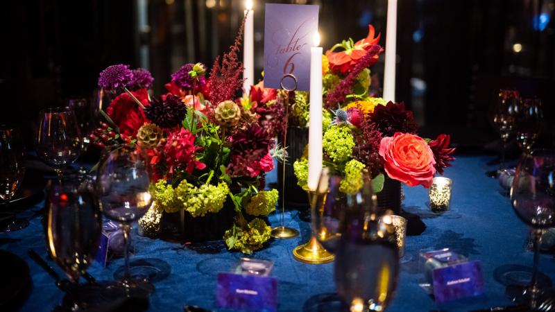 A beautiful place setting with green and pink flowers, candles, and a blue table cloth.