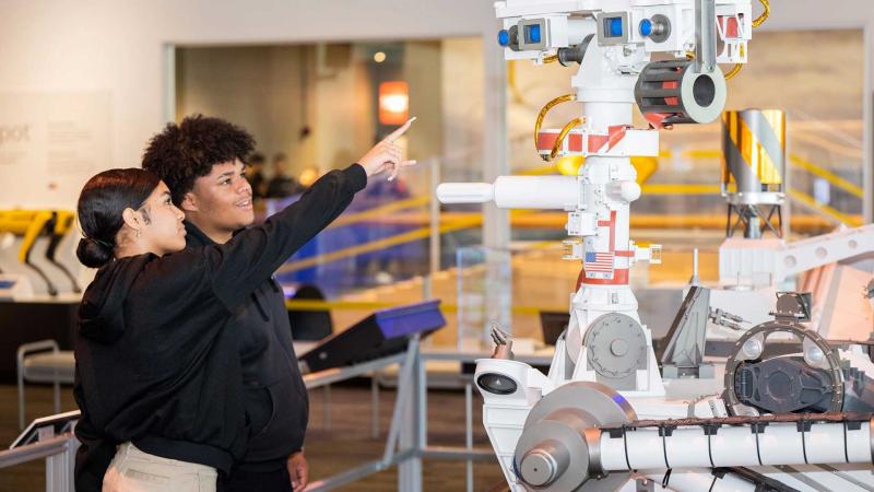 Two interns looking at the Mars rover in the Exploring AI exhibit.