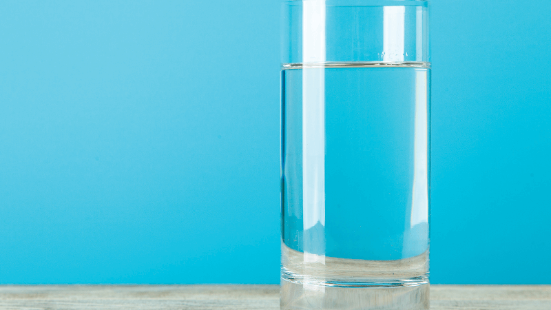 A glass of water on a table against a blue background