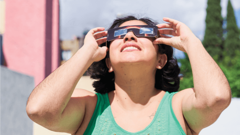 A woman holds eclipse glasses up to her eyes while she views the sun
