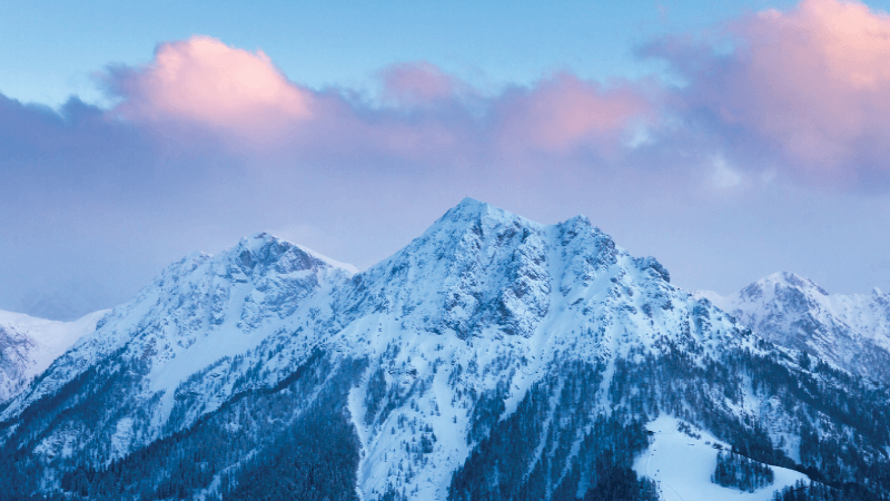 A mountain covered in snow and surrounded by pink clouds