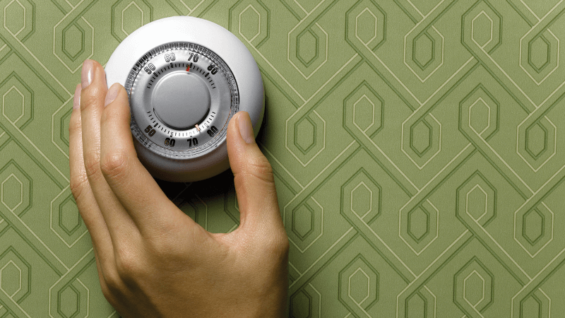 A hand adjusts a thermostat on a green wall
