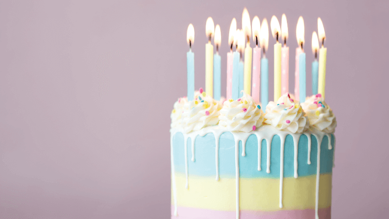 A pastel birthday cake covered in candles on a light pink background