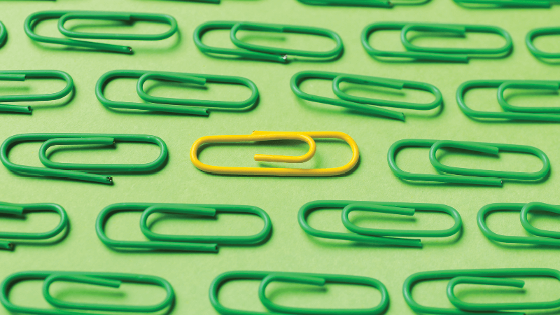 Green paper clips with one yellow paper clip on a green background