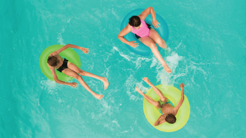 Three children sit in colorful inner tubes in a pool