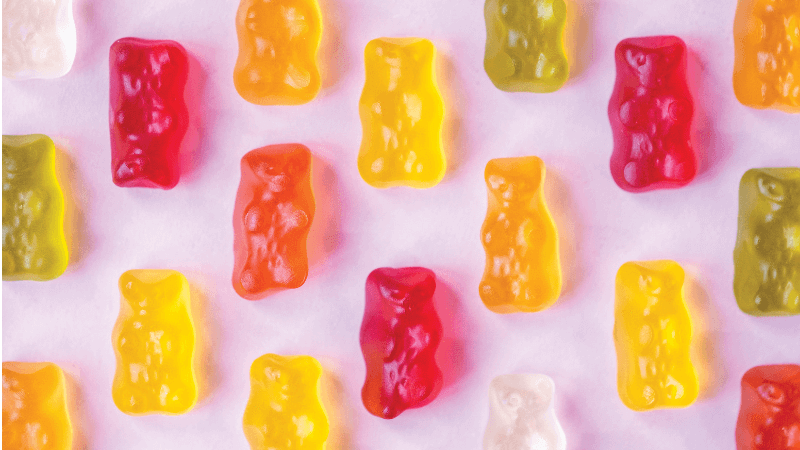 Different colored gummy bears on a light pink background