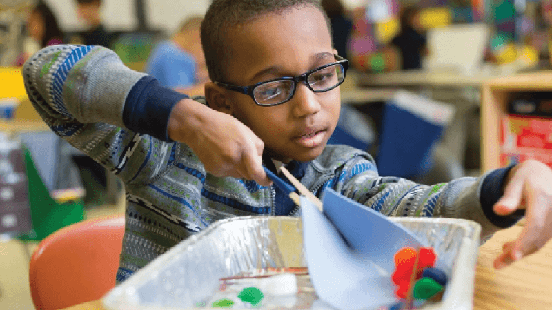 A student scoops items in a classroom during and engineering activity.