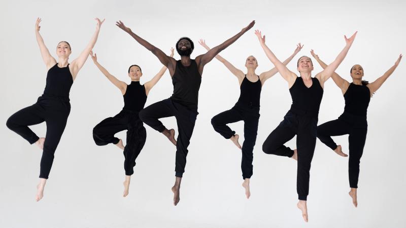 Dancers from SYREN Modern Dance appear in black uniforms in front of a white background.