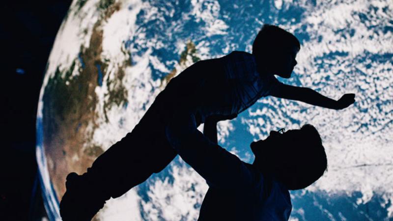 A parent holding up their child, silhouetted in front of the Gaia Globe.