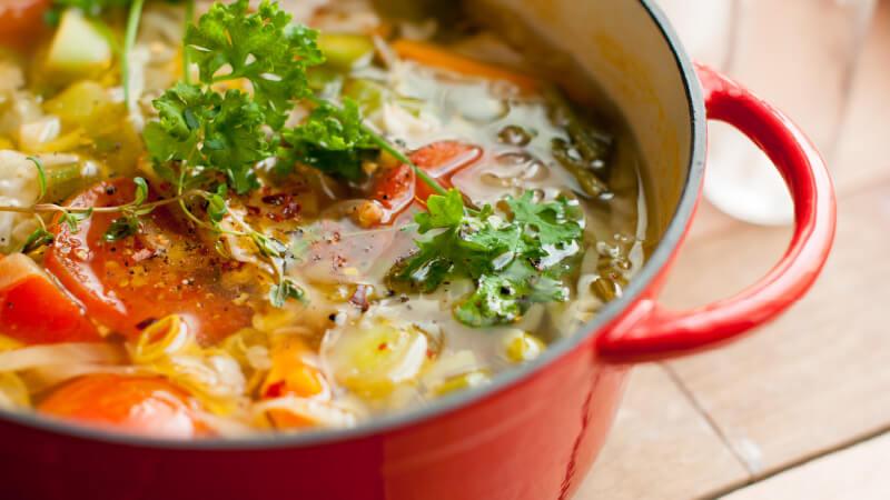 A close up photo of a hearty coup with broth and vegetables.