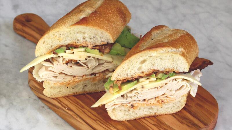 A sandwich on ciabatta bread with turkey, bacon, avocado, and cheese.