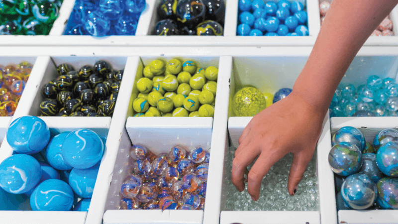 A hand reaches from marbles sorted by color and size