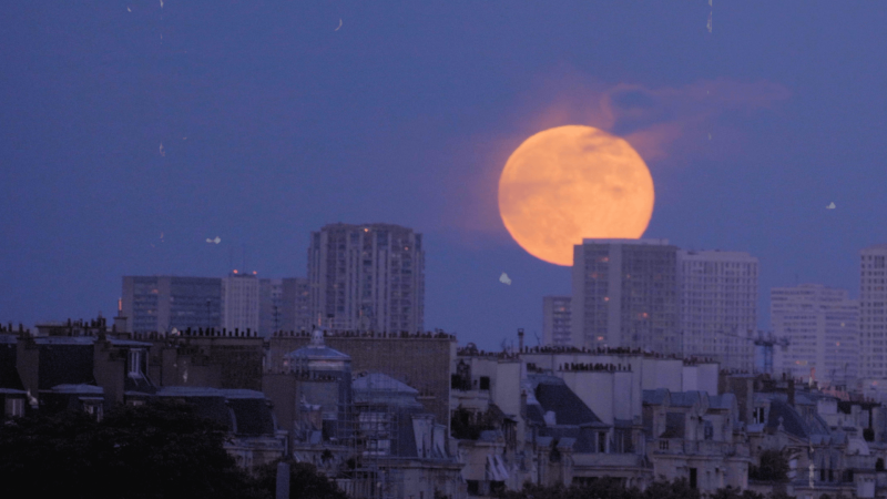 Picture of full moon rising over a city.