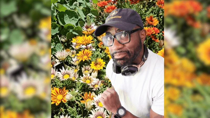 Maynard Okereke smiling in front of a flower garden