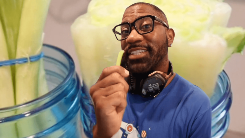 Maynard Okereke holding a green onion in front of green onion and celery stems in jars