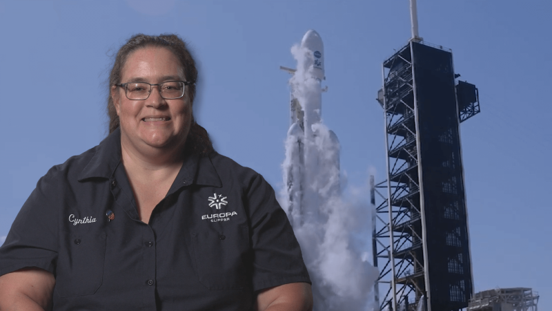 Dr. Cynthia Phillips in front of an image of the Europa Clipper launch