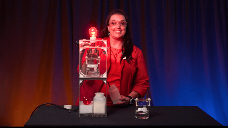 Museum Educator Karen demonstrating the conductivity of water with a circuit and a light bulb