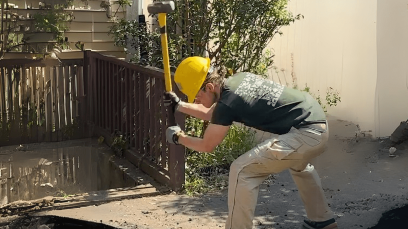 A person breaking up asphalt with a sledgehammer