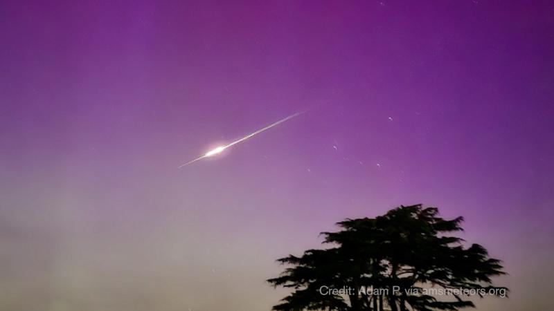 A large bright comet travels across a purple sky.