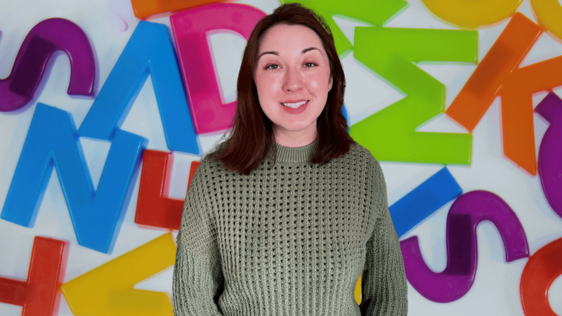 Alex Dainis in front of an assortment of rainbow colored letters.