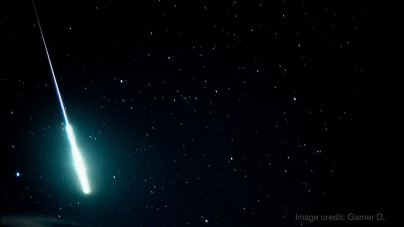 A fireball glows green and blue as it shoots across a dark sky.