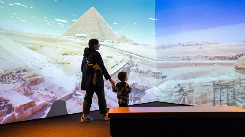 A mother and son look at a landscape of the Pyramids of Giza.