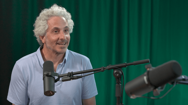 Keith Ellenbogen talking into a microphone in front of a green curtain
