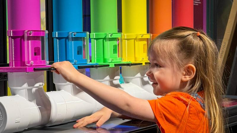 A young girl interacting with rainbow colored tubes in the Making Waves exhibit.