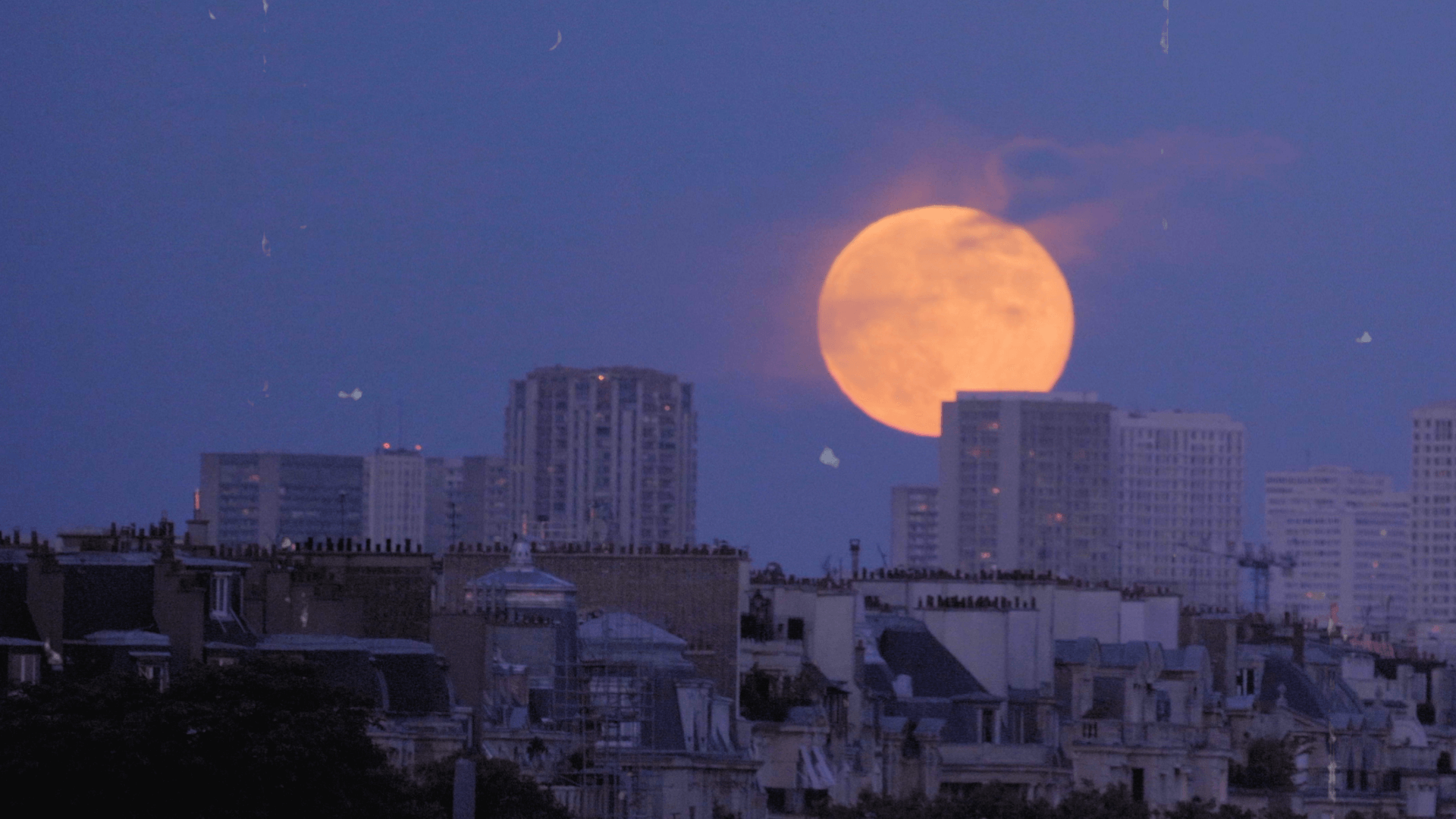 Picture of full moon rising over a city.