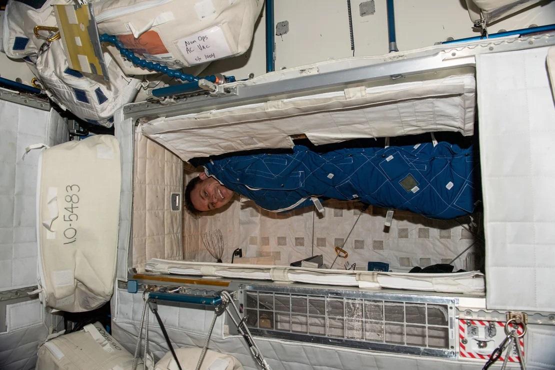 Astronaut John Cassada straps himself into a bag in his sleeping cubby, preparing for a night’s rest.