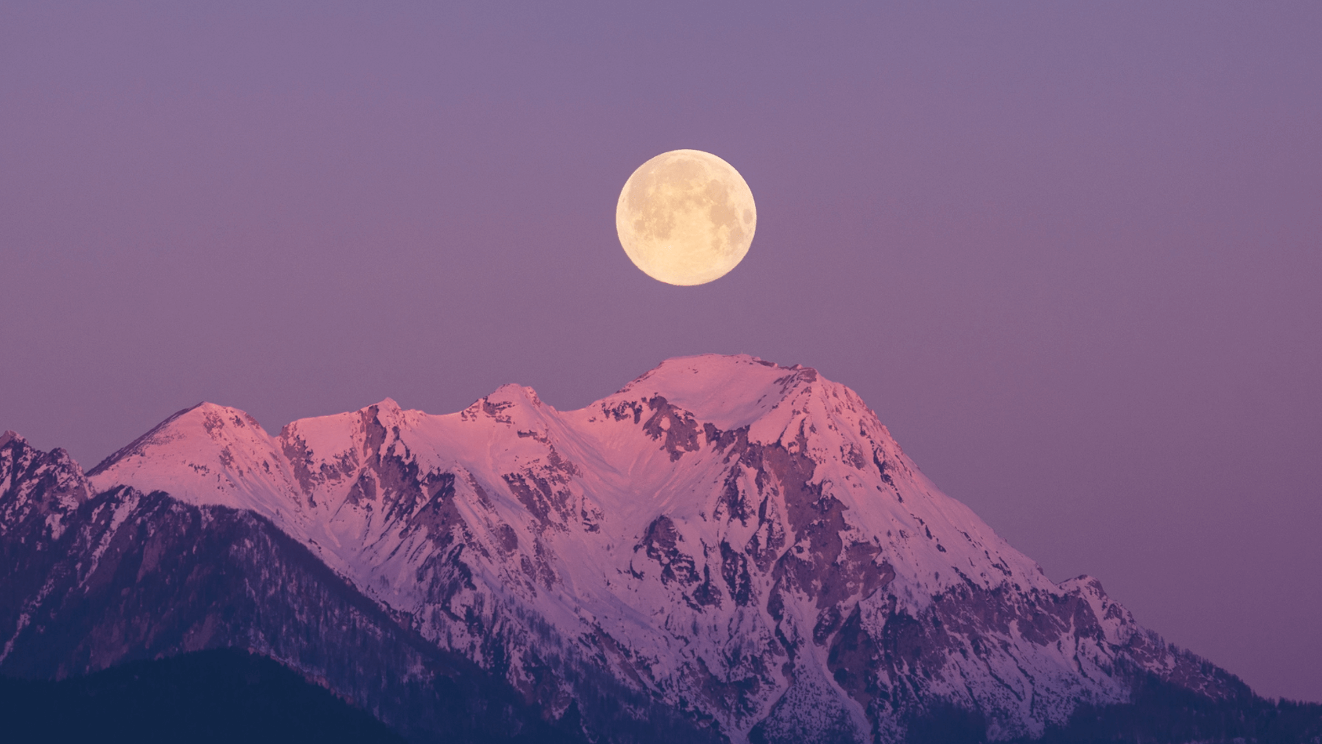 A full moon rises over a snowy mountain
