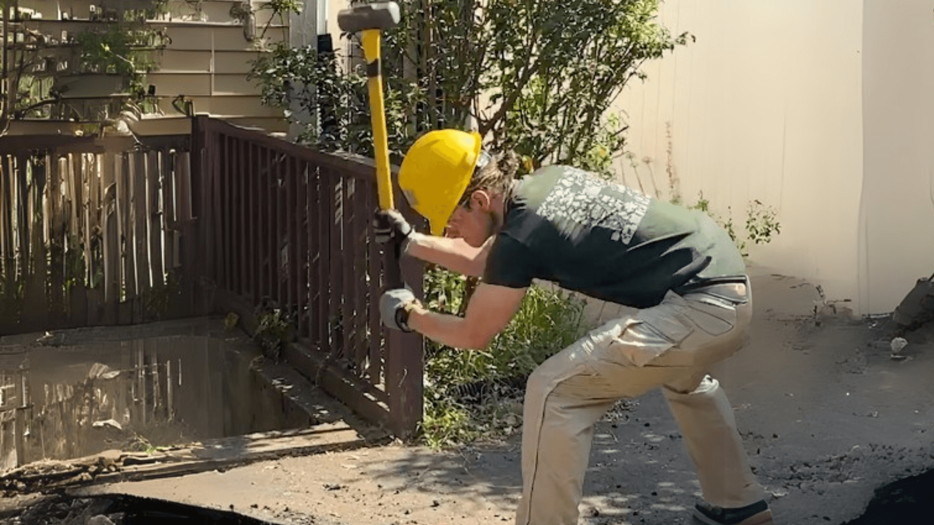 A person breaking up asphalt with a sledgehammer