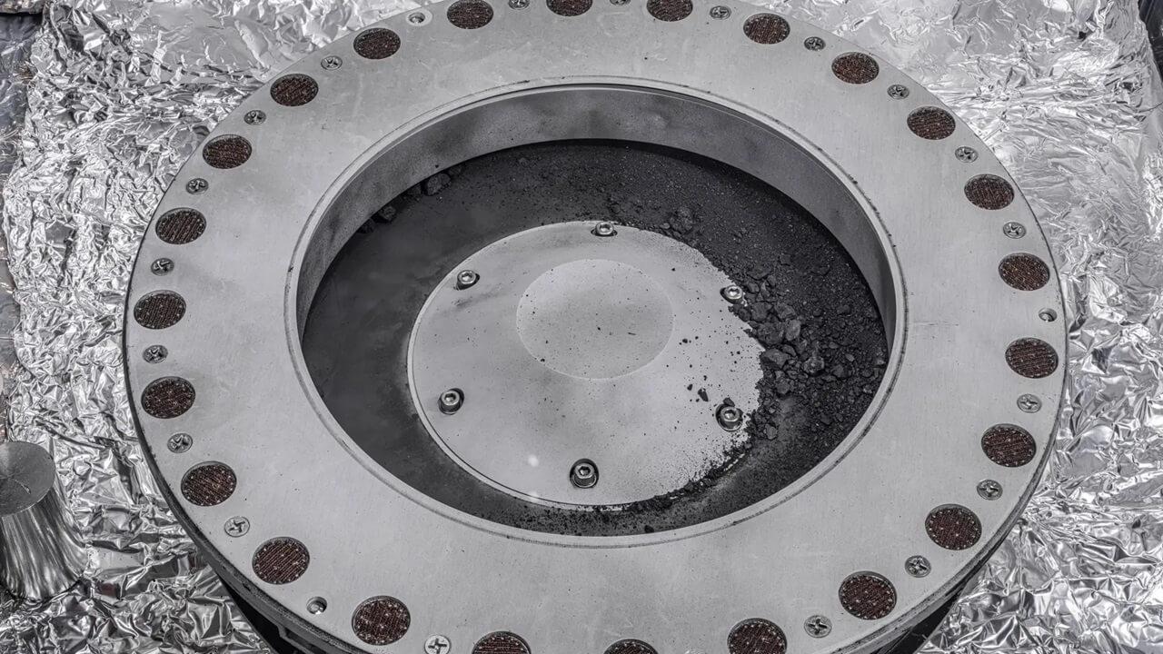 An image of the top of the sample capsule showing a bunch of material from Bennu on the outside of the capsule. Credit: NASA/Erica Blumenfeld and Joseph Aebersold