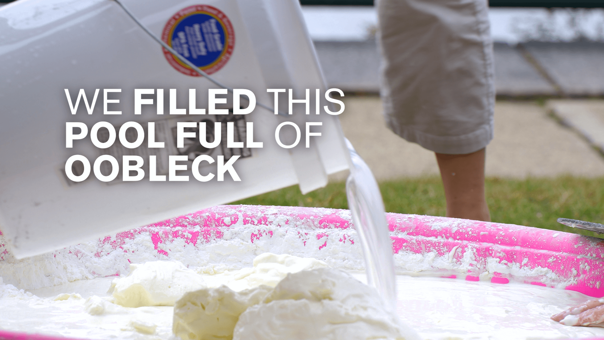A bucket of oobleck is poured into a kiddie pool with the white text "We filled this pool full of oobleck"