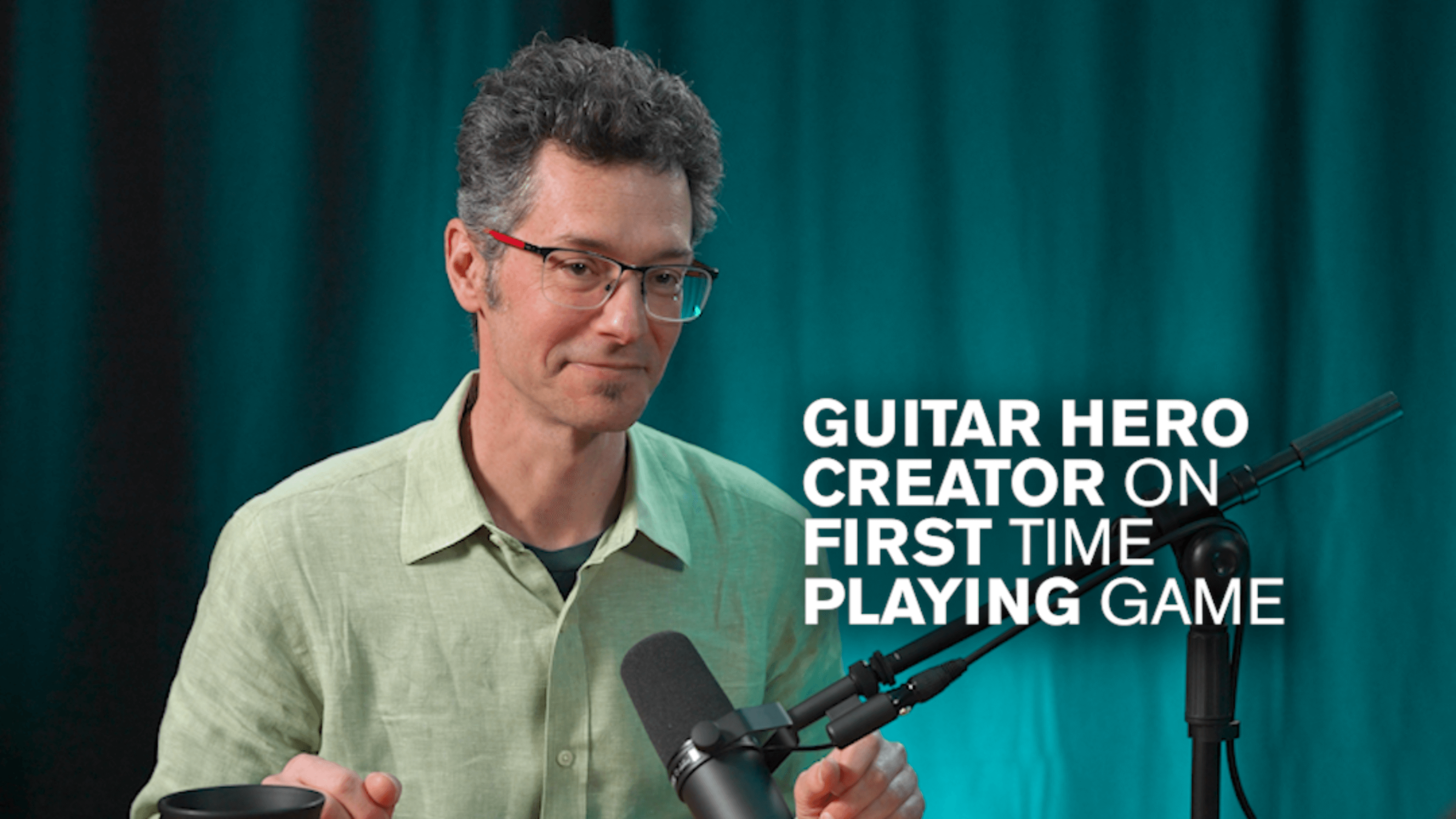 Eran Ergozy in front of a teal backdrop with white text reading "Guitar Hero Creator on First Time Playing Game"