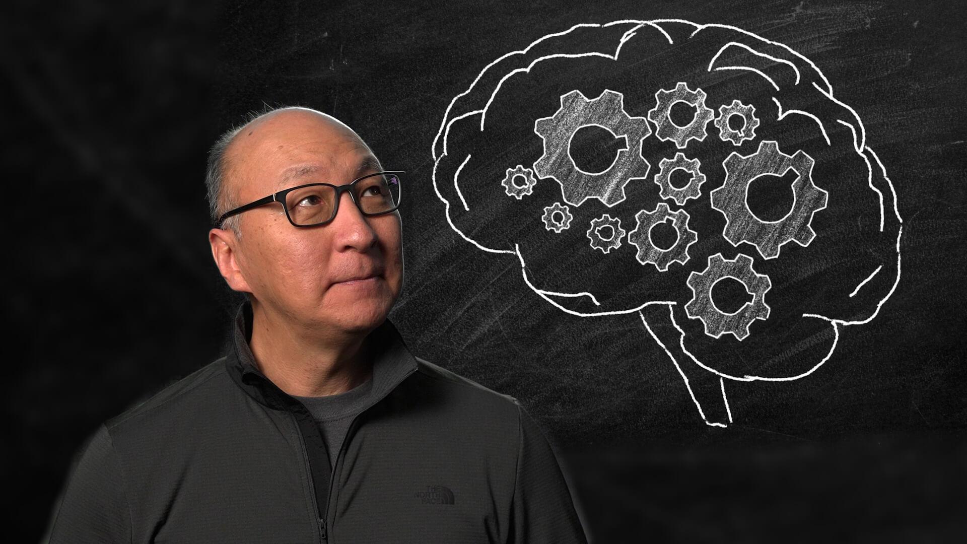 Insoo Hyun in front of a drawing of a brain on a chalk board.