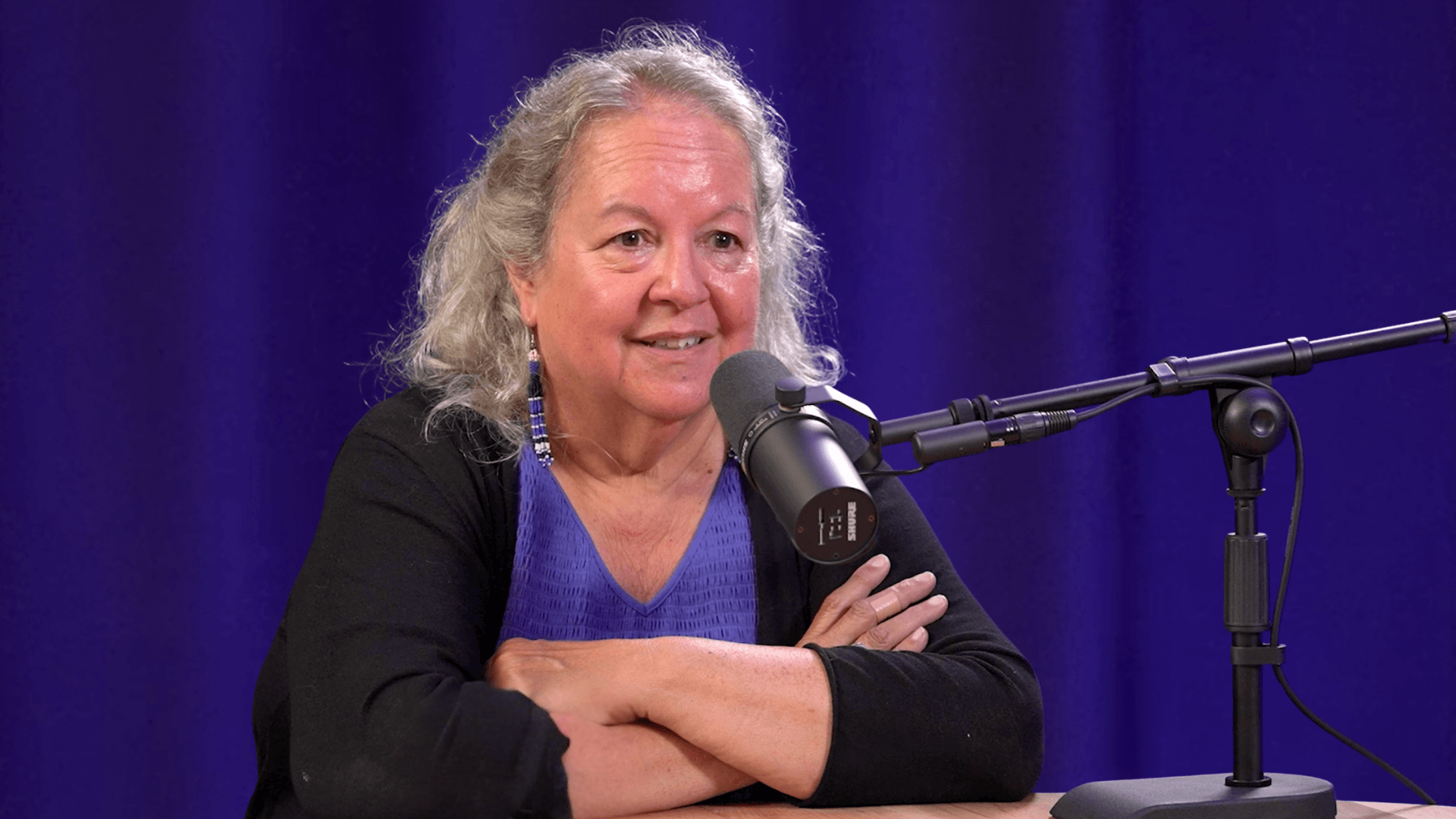 Robin Wall Kimmerer speaking into a microphone in front of a purple lit curtain.
