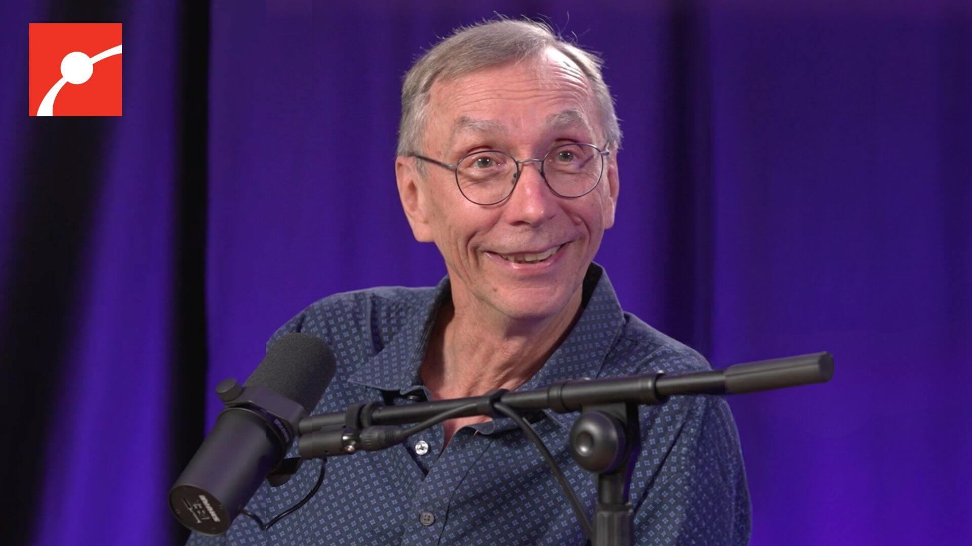 Svante Pääbo smiling in front a a curtain lit with purple light.