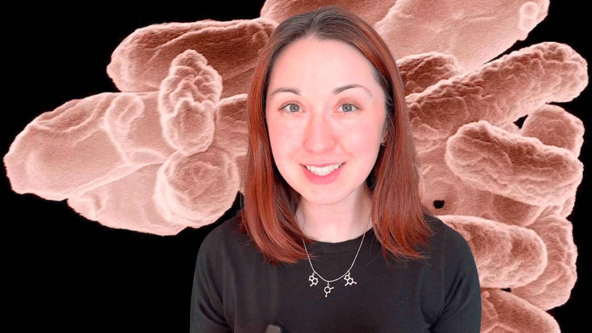 Alex Dainis in front of a microscopic view of bacteria