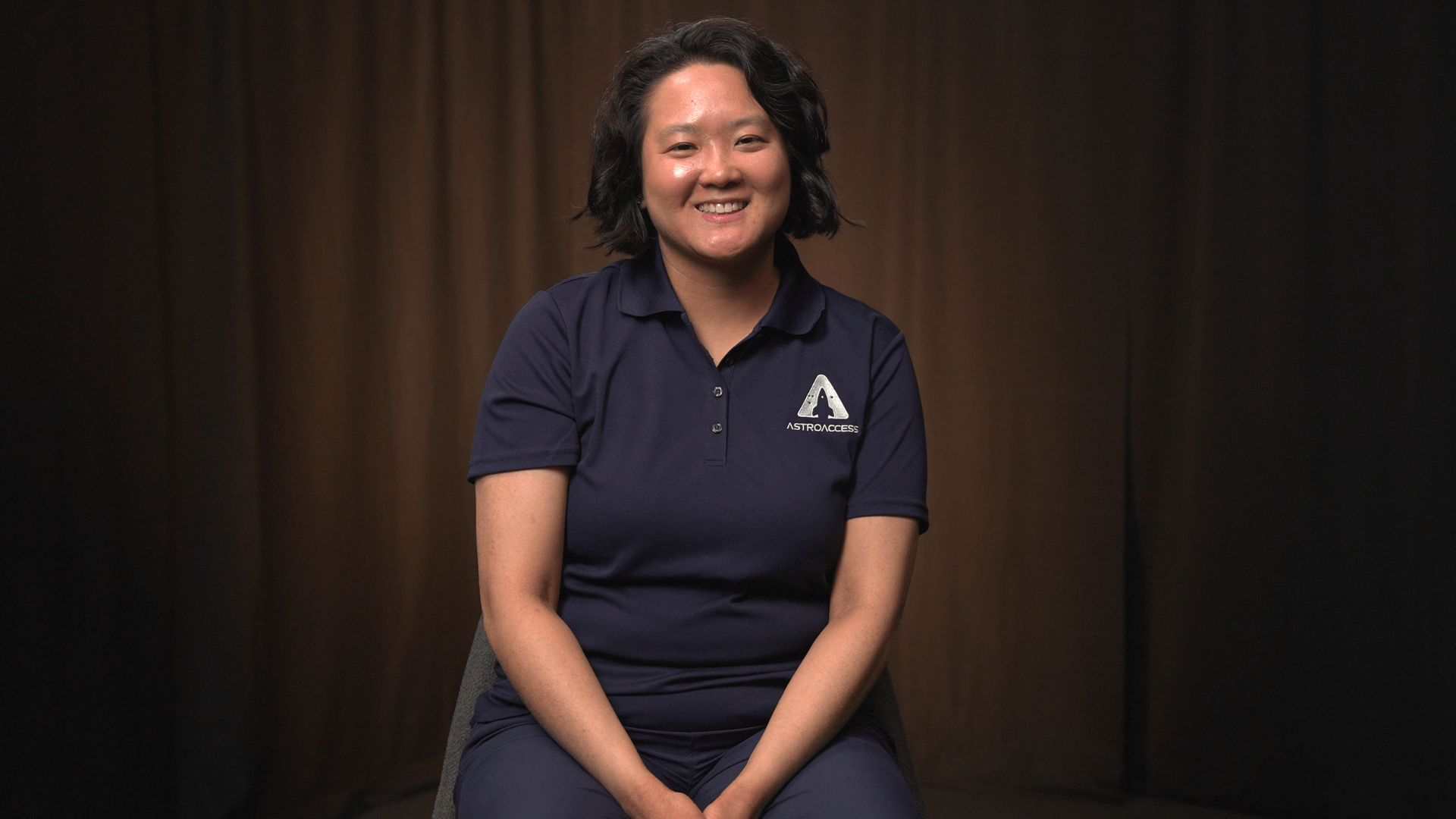 Shelia Xu smiles at the camera in front of a black curtain lit with orange light