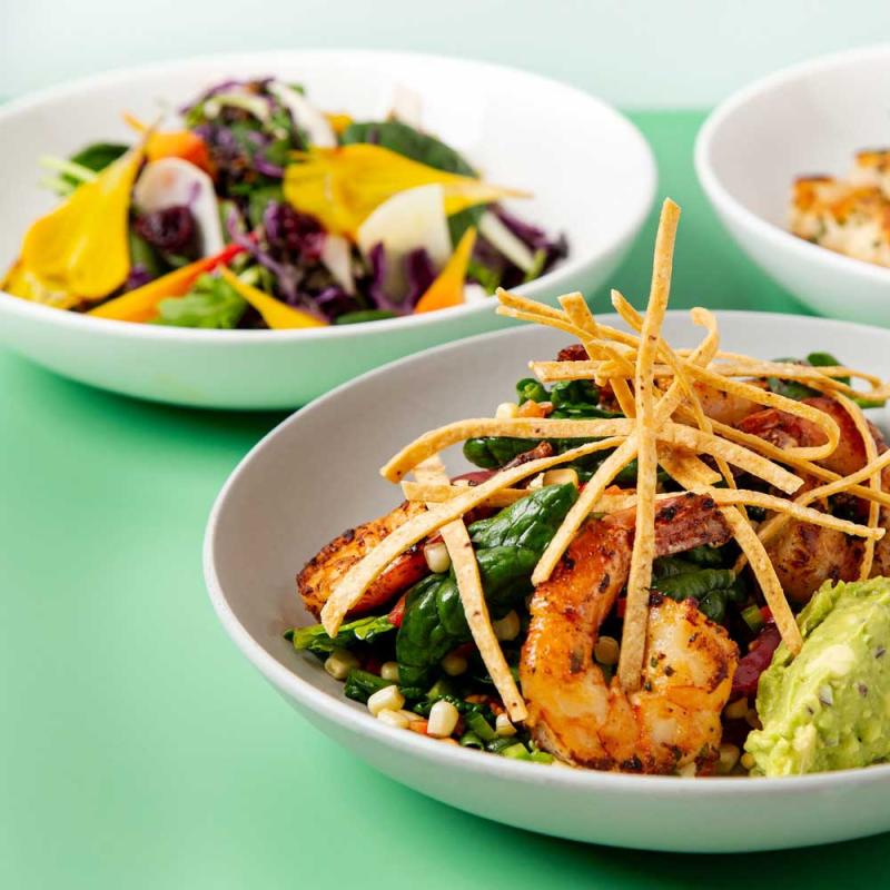 Bowls of various salads with fresh greens, shrimp, and other toppings.