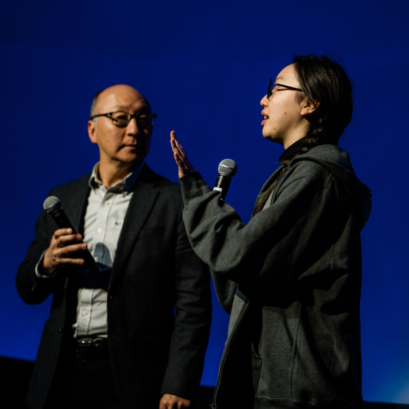 A woman speaks to a man on stage.